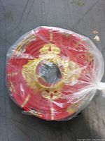 Flat-packed red paper lantern with gold Chinese designs in clear plastic