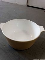 Top angled view of single beige CorningWare round casserole dish showing handles and interior