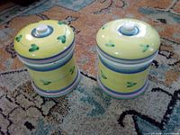 Both yellow ceramic canisters with lids showing colour, pattern and general condition