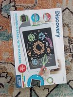 Front of box showing Discovery drawing easel, graphics of space scene, age rating, marker count