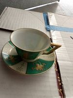 Teacup on matching saucer showing green and white panels with gold floral design
