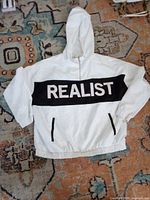 Front view of white hooded windbreaker showing REALIST panel, pockets, and overall condition