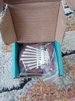 Brown wooden mini kalimba with metal tines in box, chain in plastic bag