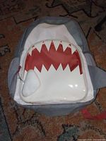 Front view of gray and white backpack showing shark teeth graphic, handle and overall wear