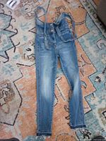 Front view of blue denim kids overalls laid flat, showing bib, straps, pockets and full pant legs