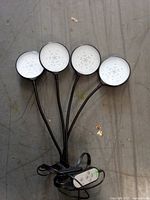 Front view showing four circular LED heads on flexible goosenecks and wired remote