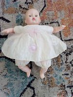 Full view of vintage baby doll in cream dress and bloomers lying on patterned rug