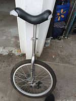 Full view of unicycle leaning against wall showing saddle, seat post, frame, wheel and pedal
