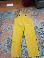 Full view of yellow CLC rain bib overalls laid flat showing size and features