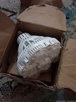 LED bulb inside opened cardboard box showing multi-lens front, side housing and screw base