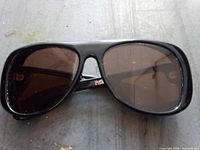Front view of sunglasses showing black frame, brown lenses and bridge logo