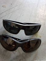 Two pairs of black wraparound sunglasses on floor