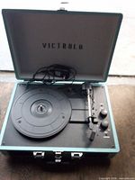 Open Victrola suitcase turntable showing platter, tonearm, controls, and charging cord