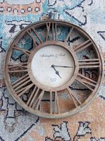 Front view of round wall clock with Roman numerals and brand text