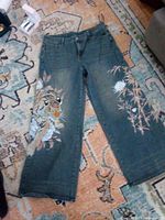 Full view of women’s denim pants laid flat showing tiger and floral print