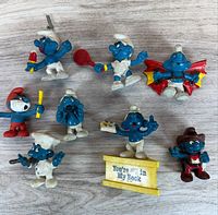 Overview of all eight Smurfs figurines and yellow stand on wood surface