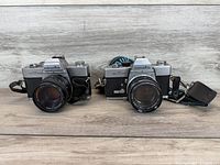 Front view of both Minolta SLR cameras showing bodies, lenses, and straps