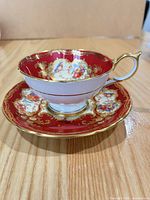 Teacup on saucer showing red ground, floral panels and gilt