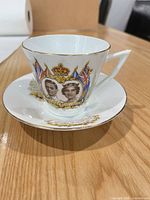 Front view of teacup on saucer displaying portraits, flags and gold trim
