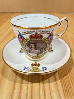 Front view of teacup on saucer showing portrait, flags, gilt detailing