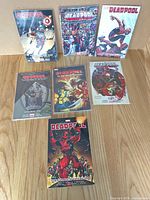 Seven Deadpool comics displayed on wood surface