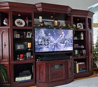 Front view of full three-piece entertainment center with TV illustrating overall design, finish, shelving, and cabinets