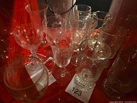 Group of etched stem glasses and handled glass mugs on red surface