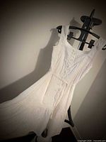Front view of white cotton sundress on hanger showing buttons and waist tie