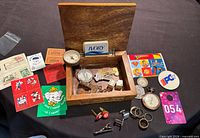 Overview of open wood box with cufflinks, tie clip, gauges, keys, dice, soap bar, patches, cards and other small items