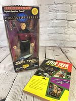 Picard figure boxed standing beside paperback book on wood surface