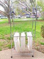Full front view of chrome garment rack with hangers and three canvas laundry bags visible
