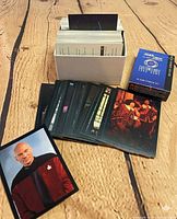 Spread of TNG white-border cards with Picard card, white storage box filled with cards, blue Star Trek 60-Card Starter Set box