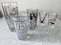 Group of three recipe tumblers and two humorous shot glasses on table