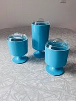 Front view of three turquoise pedestal jars with lids
