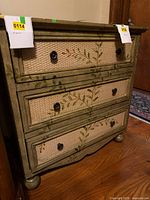 Front view showing three drawers, painted vine motif, wicker panels, metal knobs