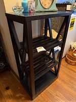 Front view of entire black wooden shelf with three slatted tiers and solid top