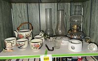 Full view of shelf showing teapot set, owl, trinket box, glass chimneys, oil lamp, doorknobs and other items
