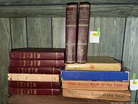 Shelf with eight burgundy Book of the Year volumes, two dictionaries, and boxed books
