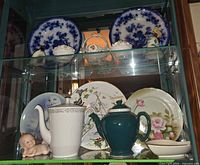 Cabinet view with two shelves of plates, teapots, figurines and dishes
