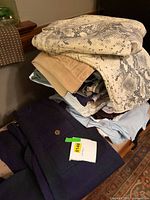 Stack of folded garments showing snakeskin jacket, khaki trousers, light blue blouse, navy jacket