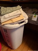 White plastic hamper with folded linens stacked on lid and shelf