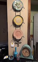 Full view showing three plates on wall rack above table holding vase, bowl, tumbler, clock