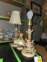 Both Hummel lamps on shelf showing figurines and lamp columns