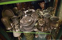 Front view showing stack of plates, mugs, bells, candlestick, coffee pot