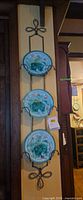 Full view of three majolica plates mounted in vertical wrought iron rack