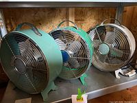 All three small metal desk fans on shelf