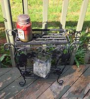 Full view of wrought iron side table with jar candle on top and crackle vase below