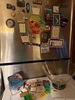 Overall view of magnets on fridge door, glass bowl with silver rim, holiday tin and matchbooks