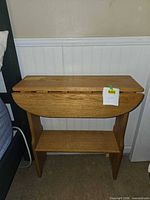 Front view of wooden drop-leaf table with leaves down, shelf visible
