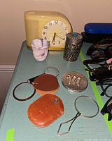 Group shot of entire lot on dresser showing clock, shot glass, pill box, magnifiers, compact, sunglasses